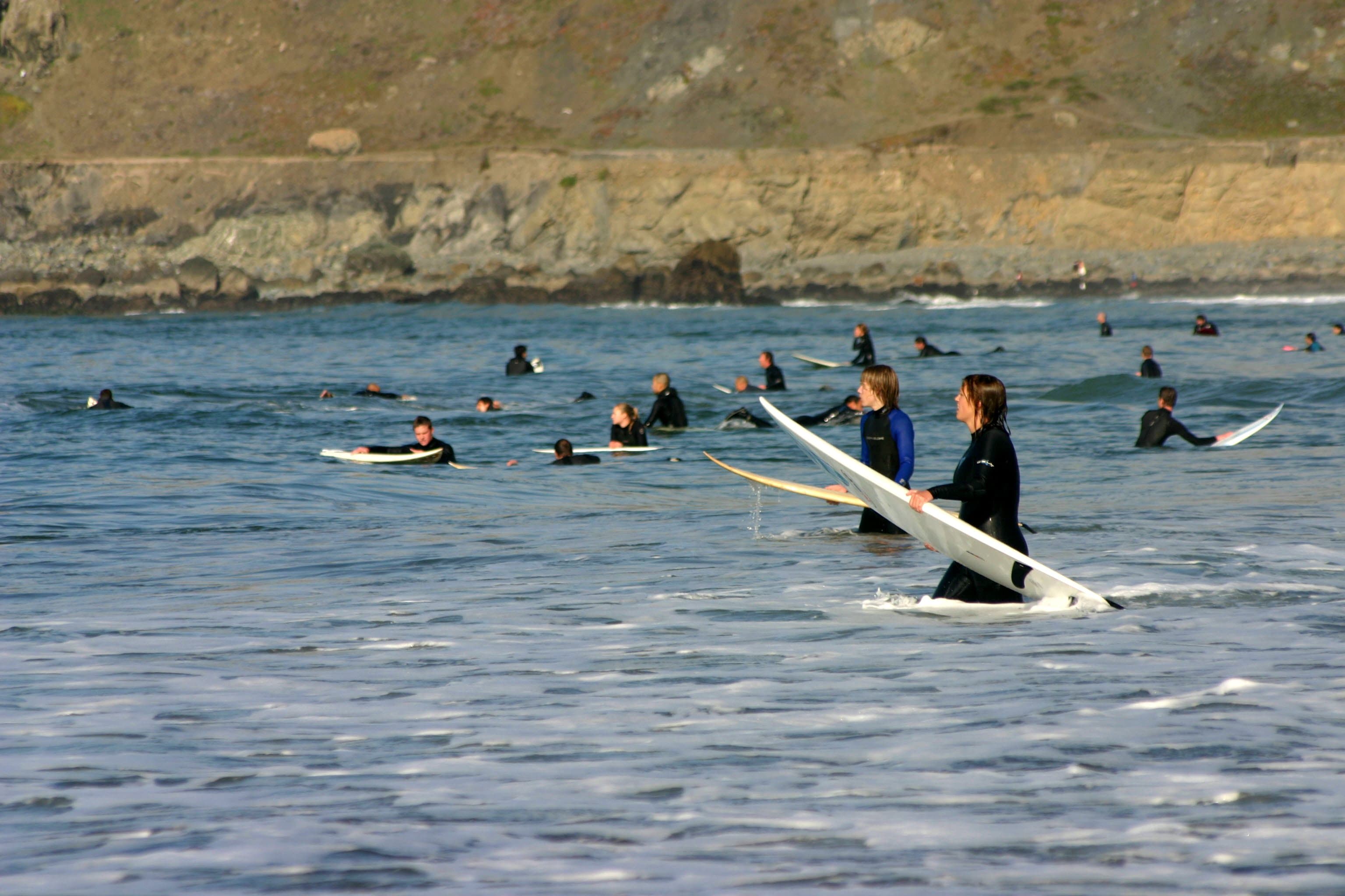Decenas de surfistas sentados en sus tablas en el pico de Pacifica, California, con un acantilado rocoso de fondo