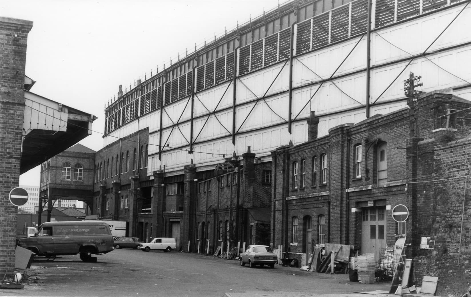 Fotografía en blanco y negro del Lower Goods Yard, en la estación de Brighton, con una hilera de edificios de ladrillo bajo la estructura de hierro de la estación.