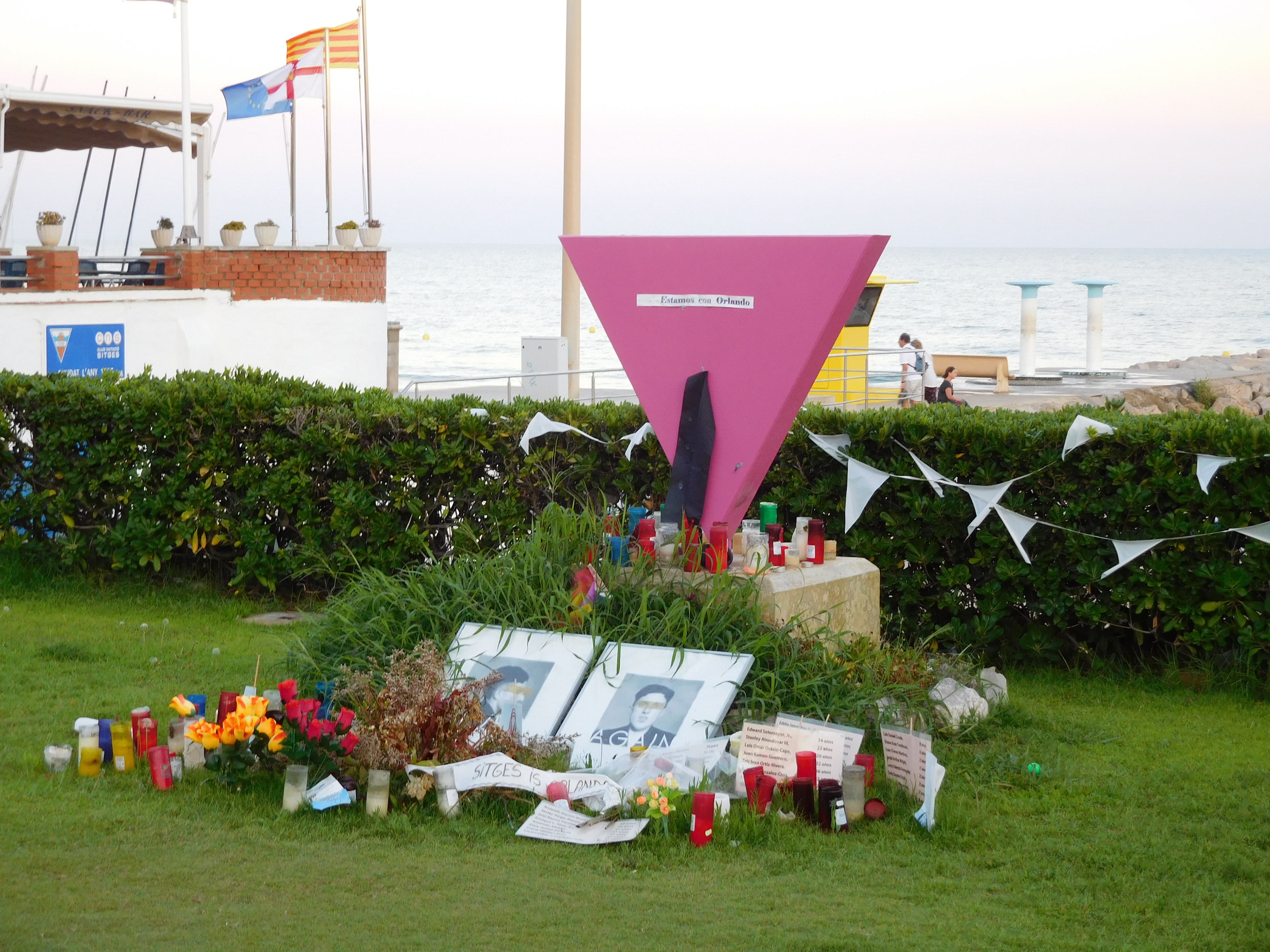 El monumento del triángulo rosa en el paseo marítimo de Sitges, con flores, velas y mensajes dejados en la base.